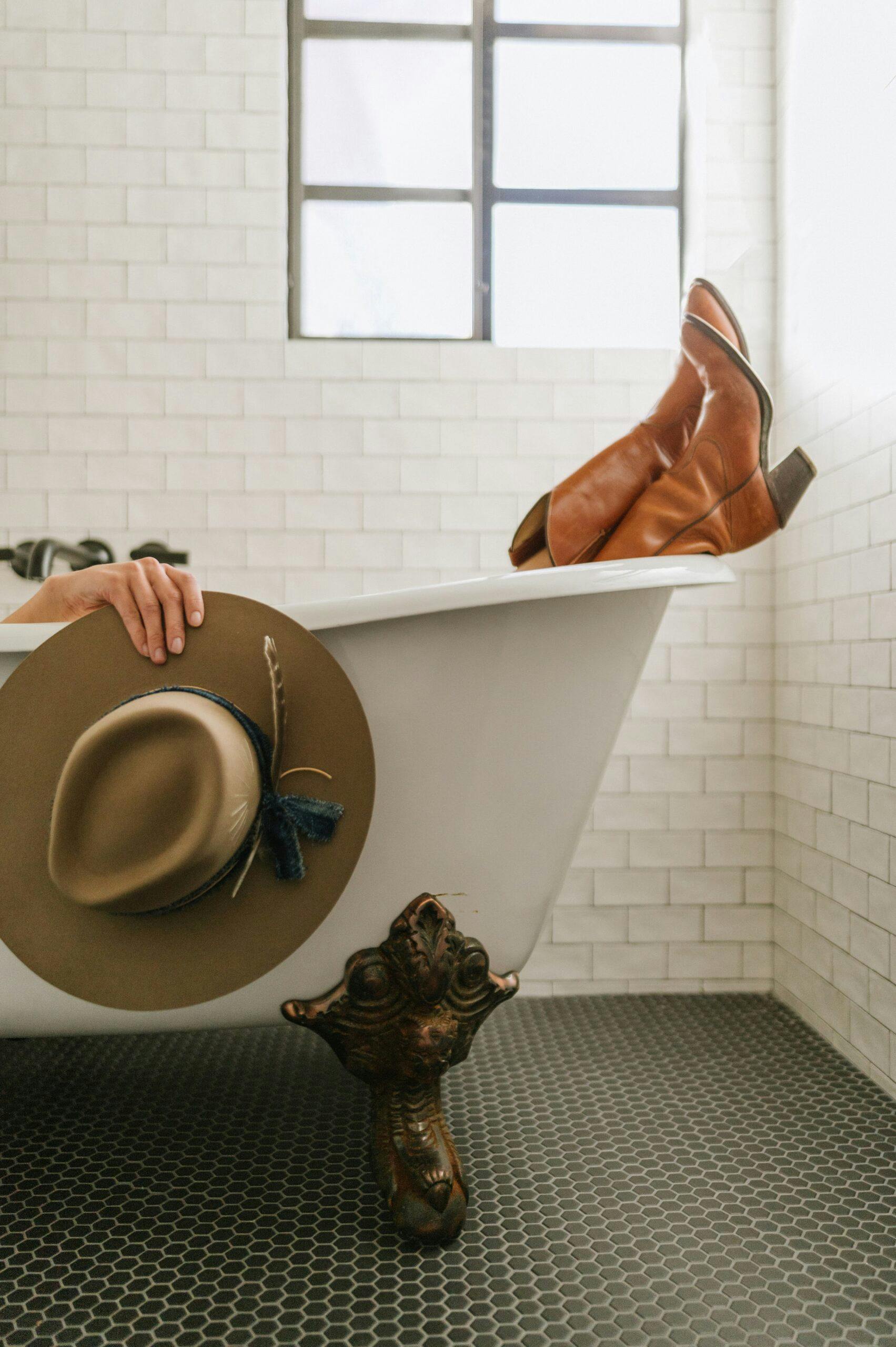 person sitting in bathtub showing cowboy boots and holding cowboy hat over tub rim